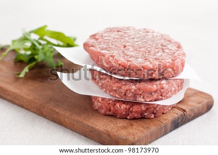 Raw burgers stacked with salad on wooden board