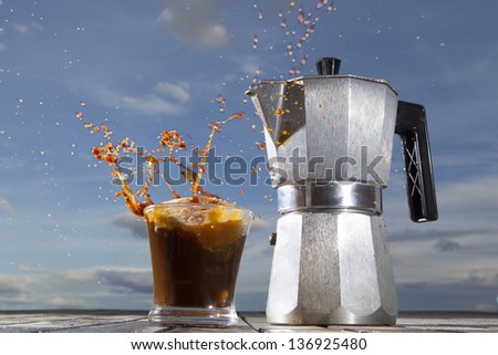 donut falling into a cup of coffee with an Italian coffee maker and sky background