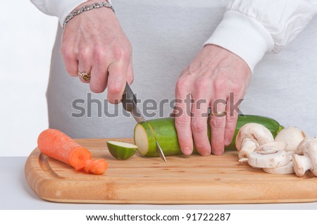A courgette being sliced on a wooden chopping board.