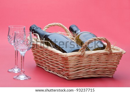 two bottles of wine in a raffia lined wicker basket with two cut crystal glasses in the shot.
