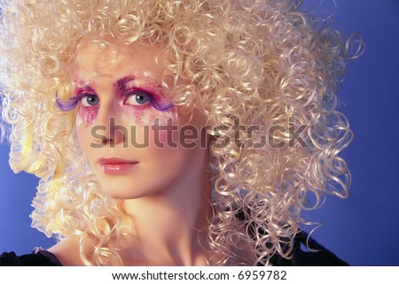 girl like a doll with curly blond hair and extravagant make-up on the blue background
