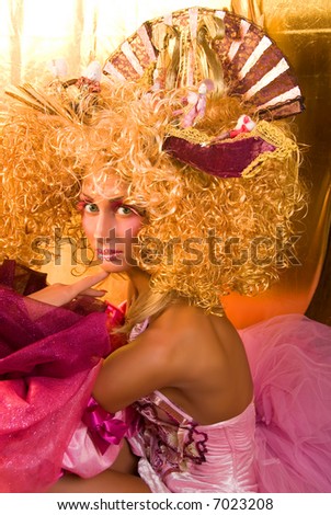 girl like a doll with curly blonde hair and extravagant make-up in medieval clothes with disguise in her hand