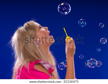 young beautiful blond inflate soap bubbles on a blue background