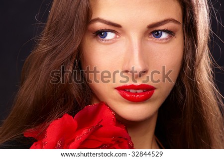 portrait of a young beautiful brunettes with red lips in a black blouse decorated with a rose