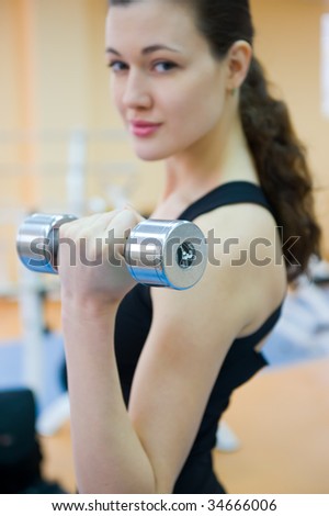 a young attractive girl swings his hands through the Dumbbell in the gym