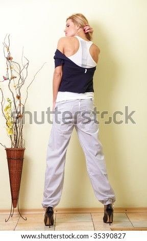 young beautiful girl in white pants and black jacket is back on a light background