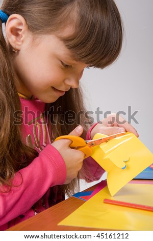 close-up of a beautiful little girl in a pink cardigan carves figures out of colored paper