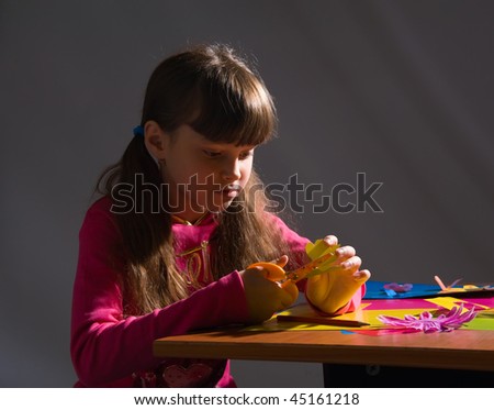 beautiful little girl in a pink cardigan carves figures out of colored paper