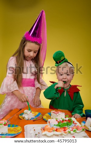 little boy in a green suit sitting at a table eating cake