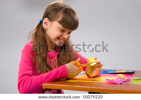 beautiful little girl in a pink cardigan carves figures out of colored paper