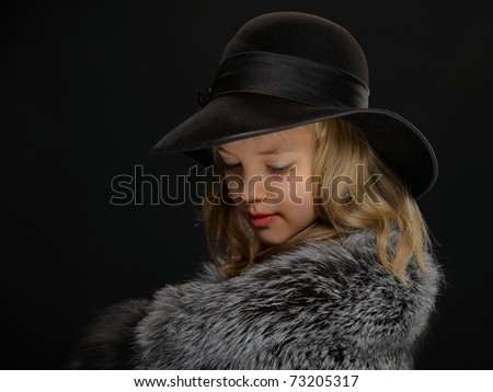 Portrait of a beautiful young lady in grey fur coat and black hat looking down on a dark background