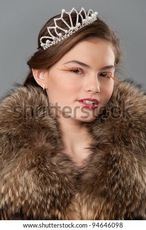 Portrait of fashion teenager model dressed in real fur and tiara with creative make-up, posing in studio