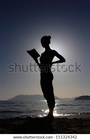 silhouette of a girl reading a book at the beach