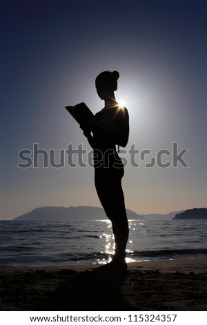 silhouette of a girl reading a book at the beach
