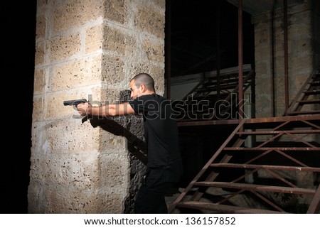 man with a gun in industrial place protect himself behind the wall