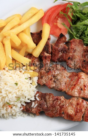 pork meat skewer served on a plate with rice and fried potatoes