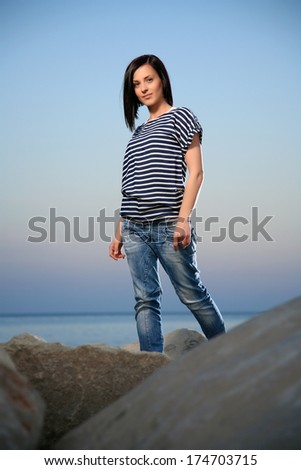 portrait of a young beautiful girl on a rocky beach with blue sky late in the afternoon