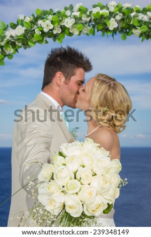 bride and groom kissing while holding a white rose flower bouquet
