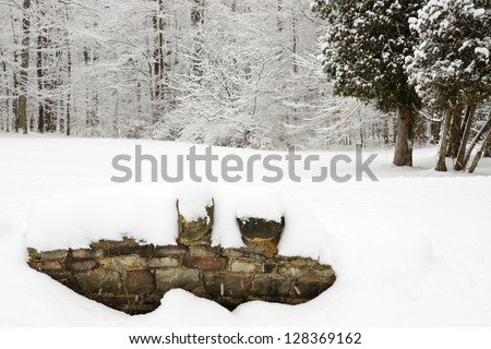 Rock wall of a bridge covered in snow and snow covered trees in winter