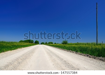 Empty bright gravel dirt road heading into distance under deep blue sky