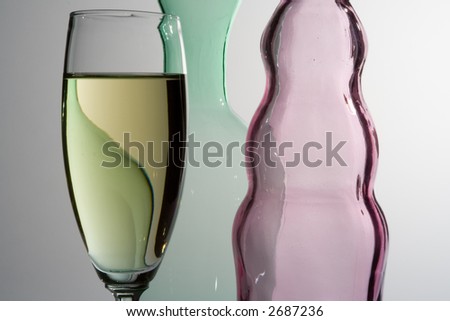 wineglass full of white wine with pink and green shaped bottles