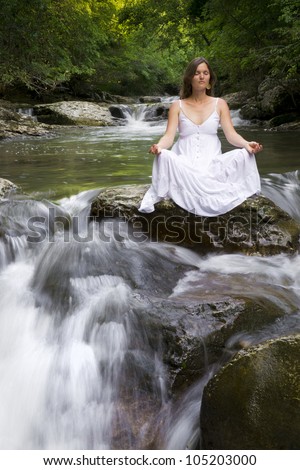 Beautiful young woman meditating surrounded by the purifying waters of a clear mountain stream