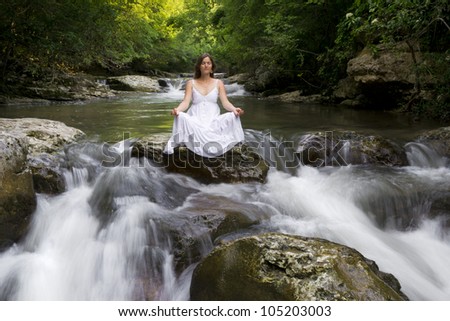 Beautiful young woman meditating surrounded by the purifying waters of a clear mountain stream