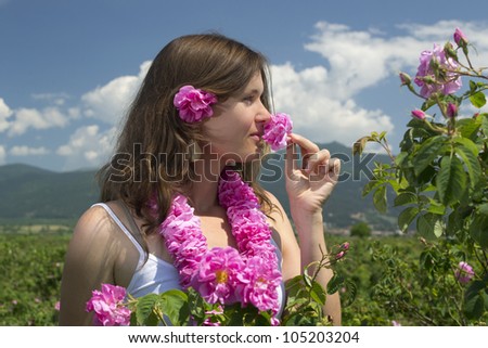Beautiful girl smelling a rose in a rose field wearing a garland of roses