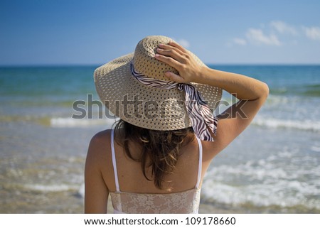 Beautiful young woman wearing a hat and a white dress enjoying the sun and the sea