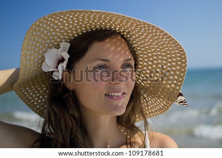 Beautiful young woman wearing a hat and a white dress enjoying the sun and the view of the sea