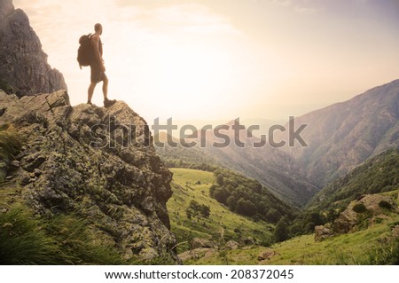 Healthy young man standing on top of a rock high in the mountains, enjoying the natural beauty in the morning light.