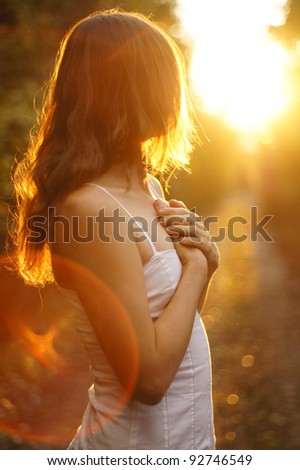 Young girl holding her hands on her heart looking towards the setting sun - stock photo