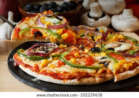 lifted Vegetarian pizza slice with a topping of Mushroom, Tomatoes, peppers, onions, sweetcorn and olives