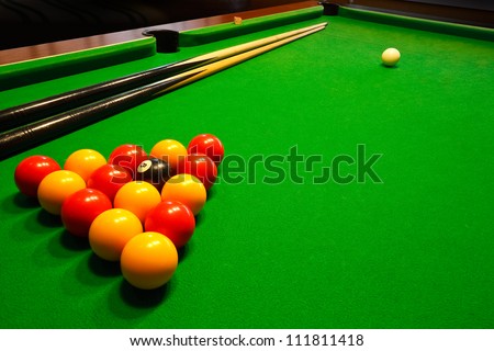 A green cloth billiards or pool table with english league red and yellow balls