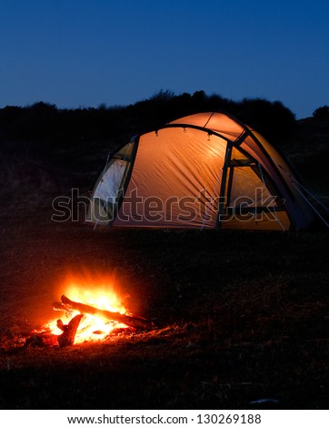 tent glows at night with campfire in front symbolizing camping holiday or vacation in the country