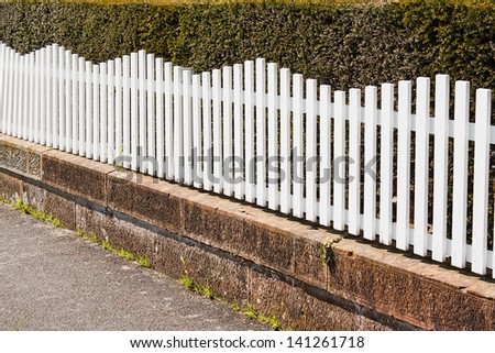 White Picket fence next to pathway with bush behind
