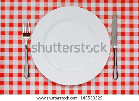Empty plate setting with plate, knife and fork on red gingham background popular symbol for diners and cafes