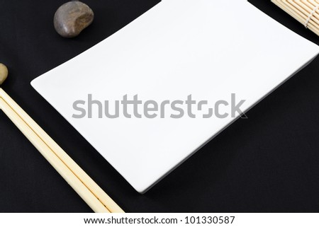 Oriental Table Set-Up - Table set-up with rectangular platter, chopsticks, pebbles and straw mat on a black tablecloth. Shallow DOF.