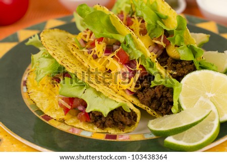 Beef Tacos - Mexican minced beef hard-shell tacos with salsa, cheese and lime wedges on a colourful plate.