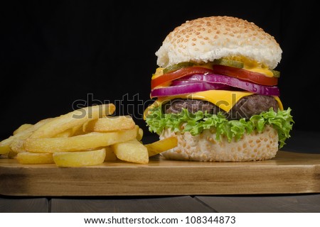 Gourmet Cheeseburger & Chips - Burger and thick cut chips on a black background. Low key lighting.