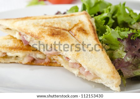 Bacon & Cheese Toastie served with salad on a white background. Close up.