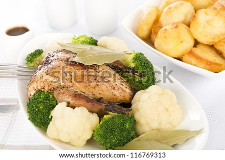 Roast Dinner - Roast partridge served with cauliflower, broccoli, roast potatoes and a jug of gravy. Traditional British Sunday and Christmas meal.