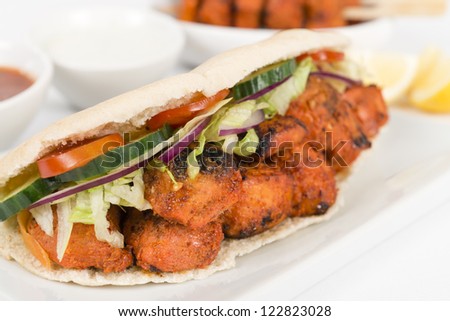 Chicken Tikka Kebab - Tandoori chicken tikka with salad in a pita bread. Served with chilli sauce, yoghurt and lemon wedges on a white background.