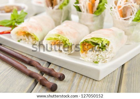 Goi Cuon - Vietnamese fresh summer rolls filled with prawns, pork, herbs, rice vermicelli and vegetables. Served with hoisin and peanut sauce dip and nuoc mam cham. Wooden background.
