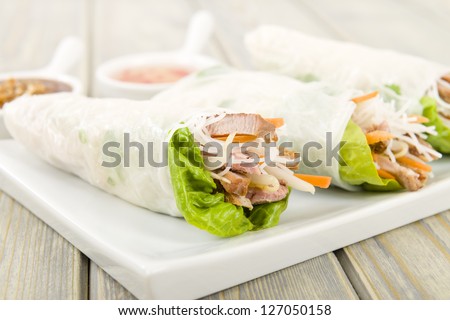 Goi Cuon - Vietnamese fresh summer rolls filled with pork, herbs, rice vermicelli and vegetables. Served with hoisin and peanut sauce dip and nuoc mam cham.  Wooden background.