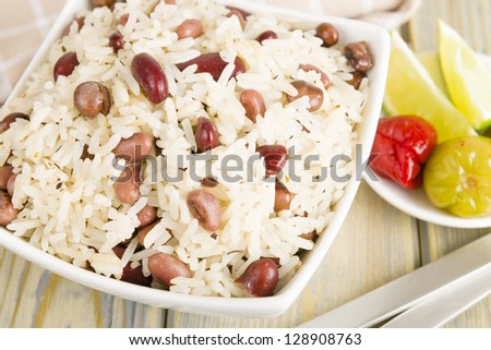 Rice and Peas - Caribbean coconut rice with red kidney beans, cowpeas and pigeon peas. Scotch bonnet chilies and lime on side. Close up.