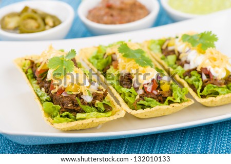 Beef Tacos - Shredded beef taco trays topped with salsa, sour cream and grated cheese. Refried beans, guacamole and jalapeÃ?Â±os in background