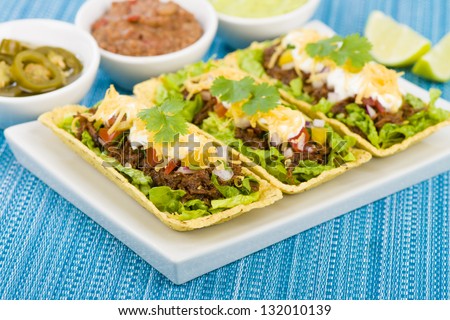 Beef Tacos - Shredded beef taco trays topped with salsa, sour cream and grated cheese. Refried beans, guacamole and jalapeÃ?Â±os in background