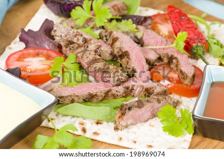 Grilled Beef Wraps - Griddled sirloin steak, sliced and wrapped in a flatbread served with blue cheese sauce and salad. Close up.