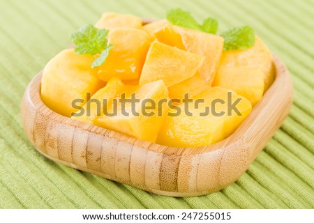 Mango - Pieces of mango in a square bamboo bowl on a green background.